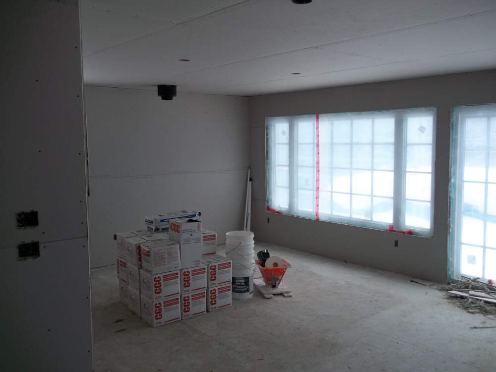 The interior of a Muskoka home construction project with gypsum wallboard hung and ready for finishing with boxes of joint compound and finishing tools standing ready for action.