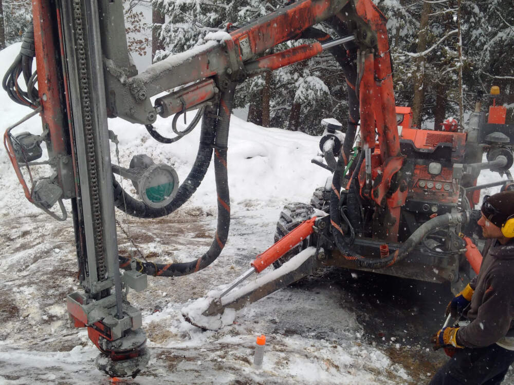 A large rock drilling machine begins driving its drill-bit into the granite bedrock on a Muskoka foundation construction site.