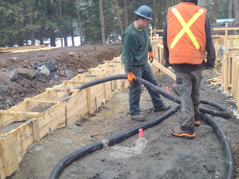 Concrete footing formwork, placement and finishing underway with a concrete line pump crew active on this Muskoka builder's construction project.