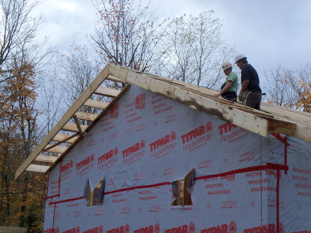 Two carpenters are engaged in assessing the wood frame structure of a roof that they are building in the Township of Algonquin Highlands, Muskoka, Ontario.