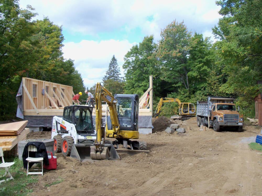 A busy homebuilding jobsite with wood framing, excavation and septic system installation underway simultaneously to represent fast-track and accelerated construction schedules.