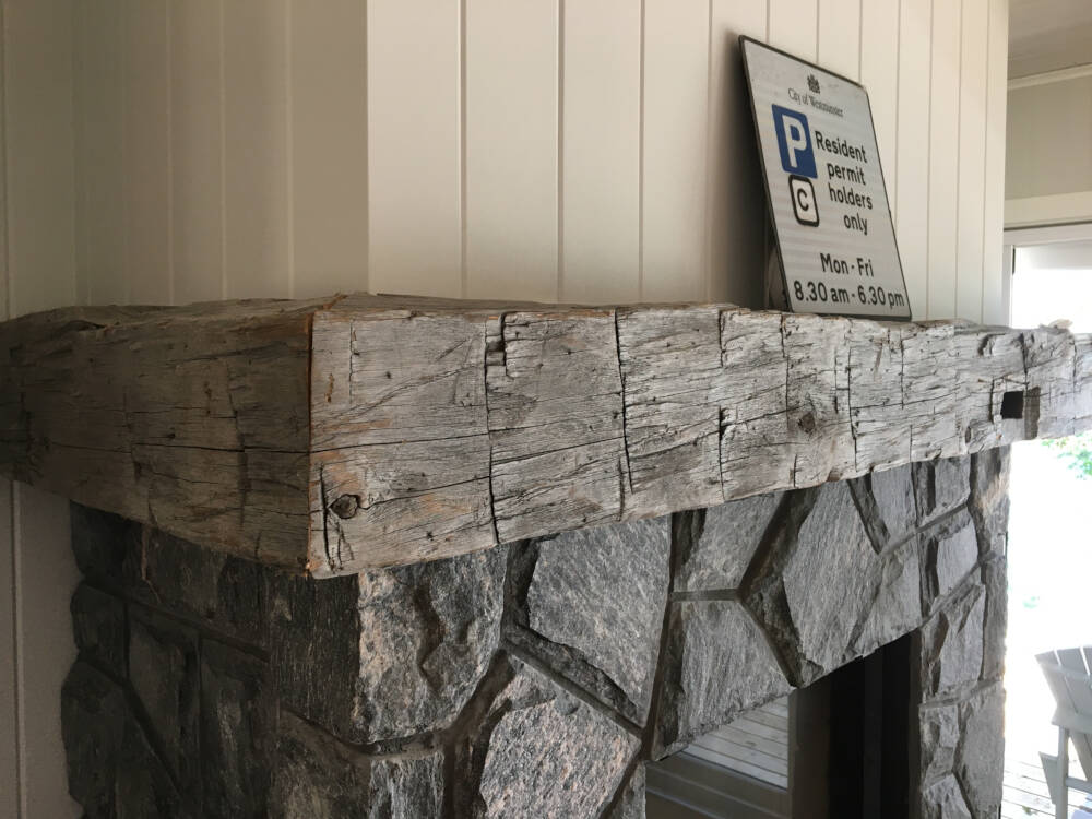 Rustic barn timber mantel above wood-burning fireplace in cottage on Lake Muskoka, Ontario.