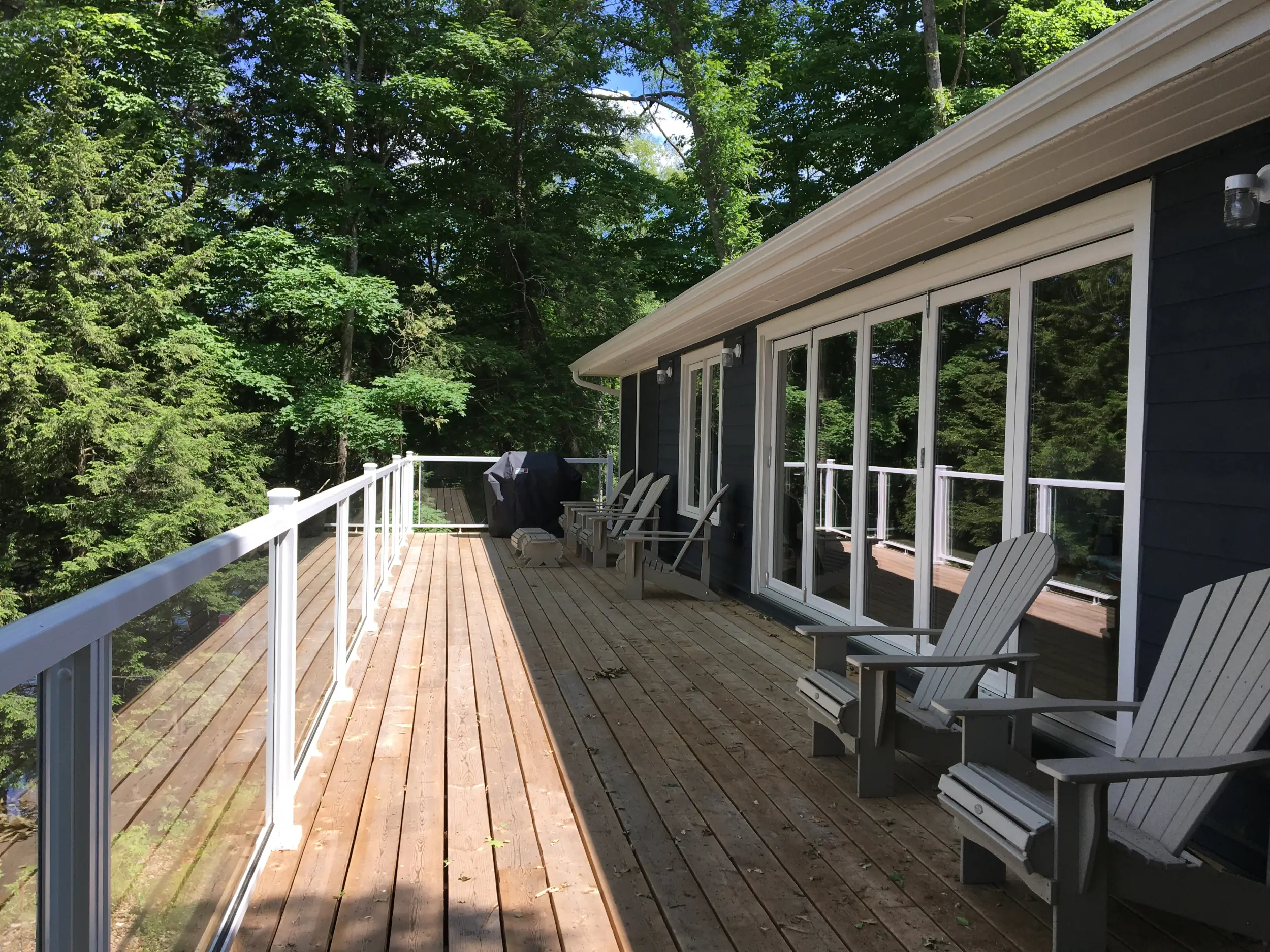 A sunny deck, Muskoka chairs and large bifolding glass doors facing Lake Muskoka.