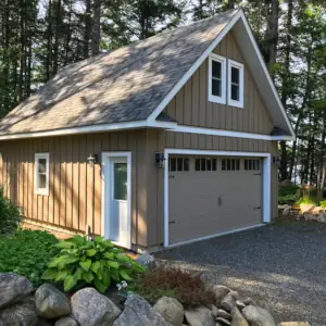 Vertical board and batten siding, white trim and a large overhead door with clear glass match this garage to the cottage on this property in Township of Lake of Bays, Muskoka, Ontario.