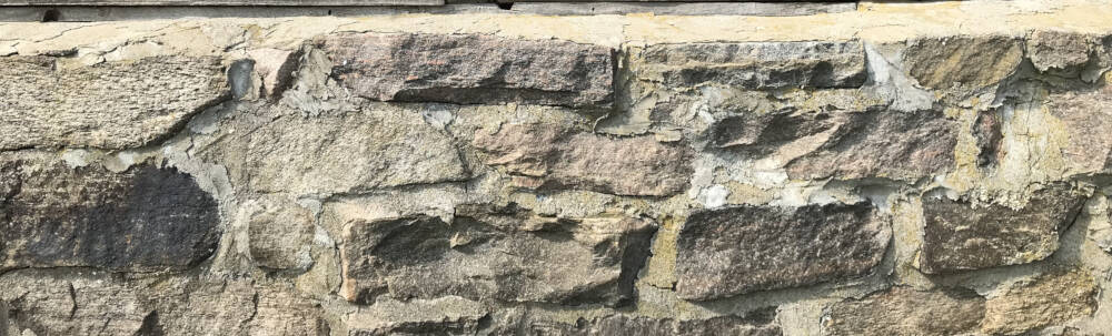 A fieldstone (or random coursed stone) masonry foundation wall supports a Muskoka, Ontario farm building.